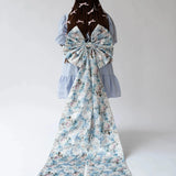 Back view of Alice Blue Josephine Midi Dress with oversized floral bow accessory. Blue midi dress styled with dramatic floral train.