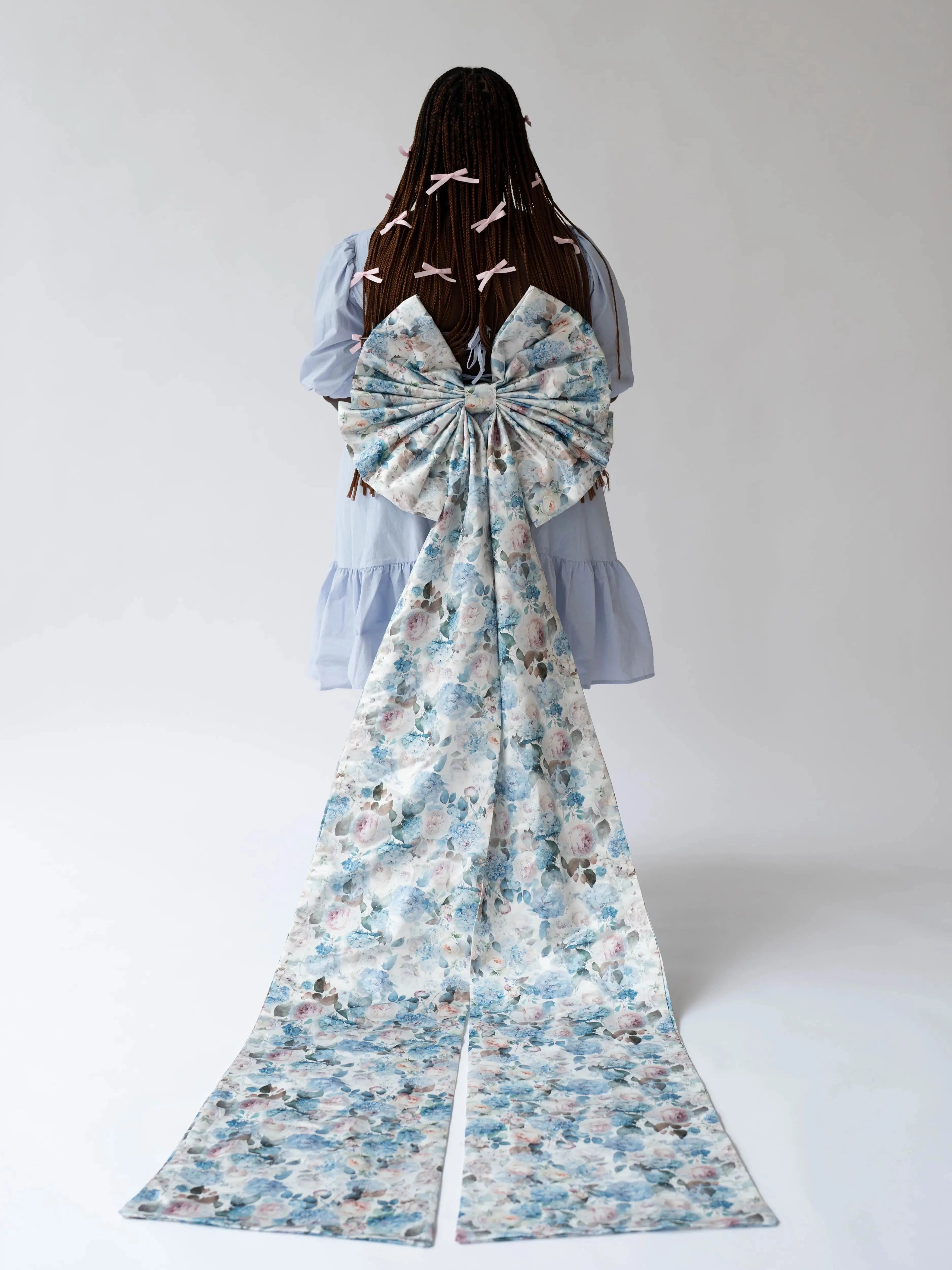 Back view of Alice Blue Josephine Midi Dress with oversized floral bow accessory. Blue midi dress styled with dramatic floral train.