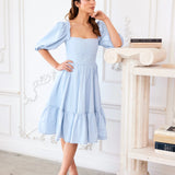 Alice Blue Josephine Midi Dress styled with puff sleeves and square neckline, worn in an elegant white room. Blue midi dress with feminine silhouette.