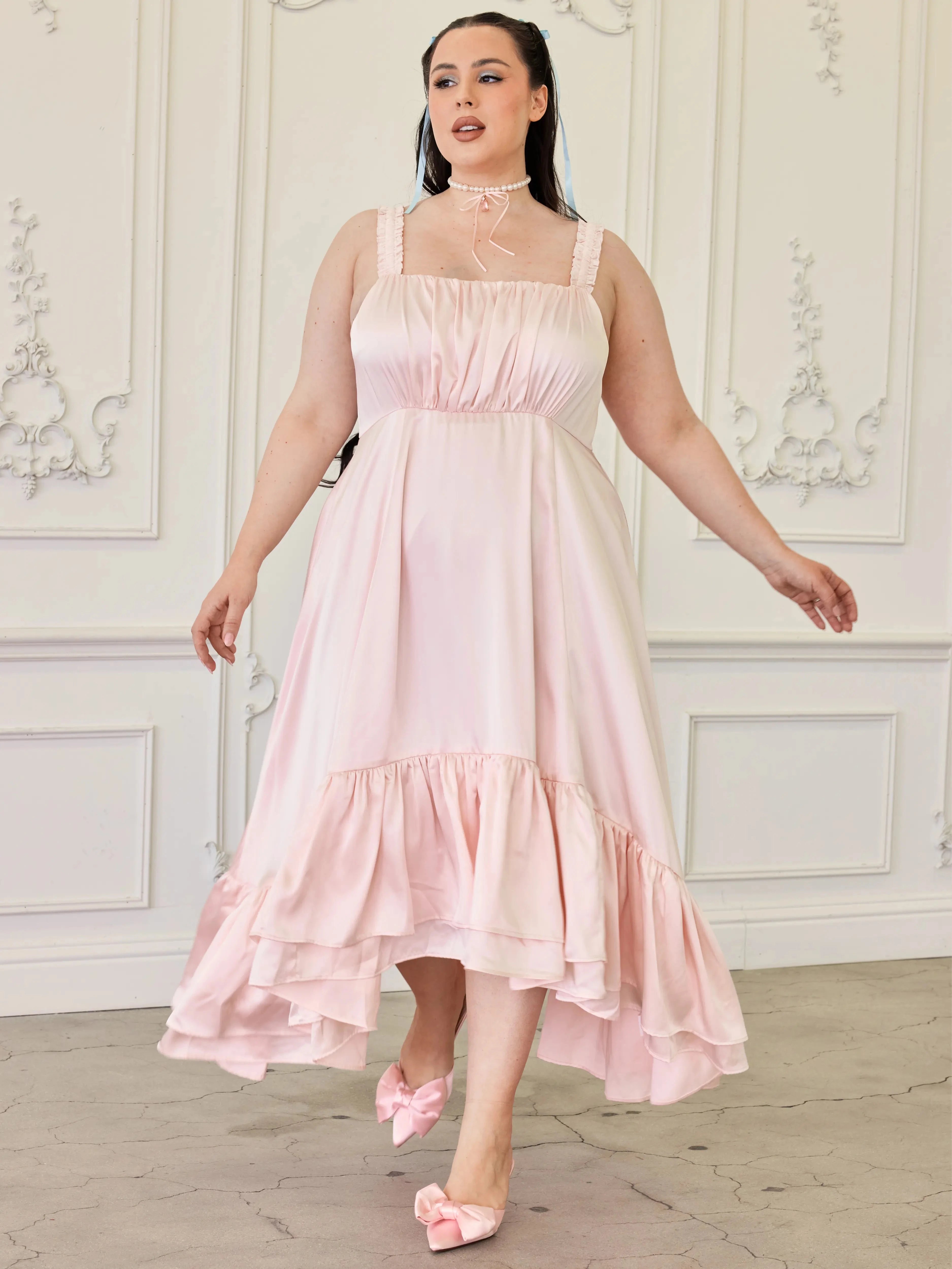 Ballerina Pink Satin Midi Dress with high-low ruffled hem and ruched bodice, modeled in a vintage room with matching pink bow heels.