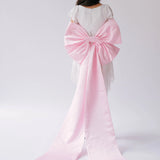 Pink satin large bow with long ribbons on a white bridal mini dress.