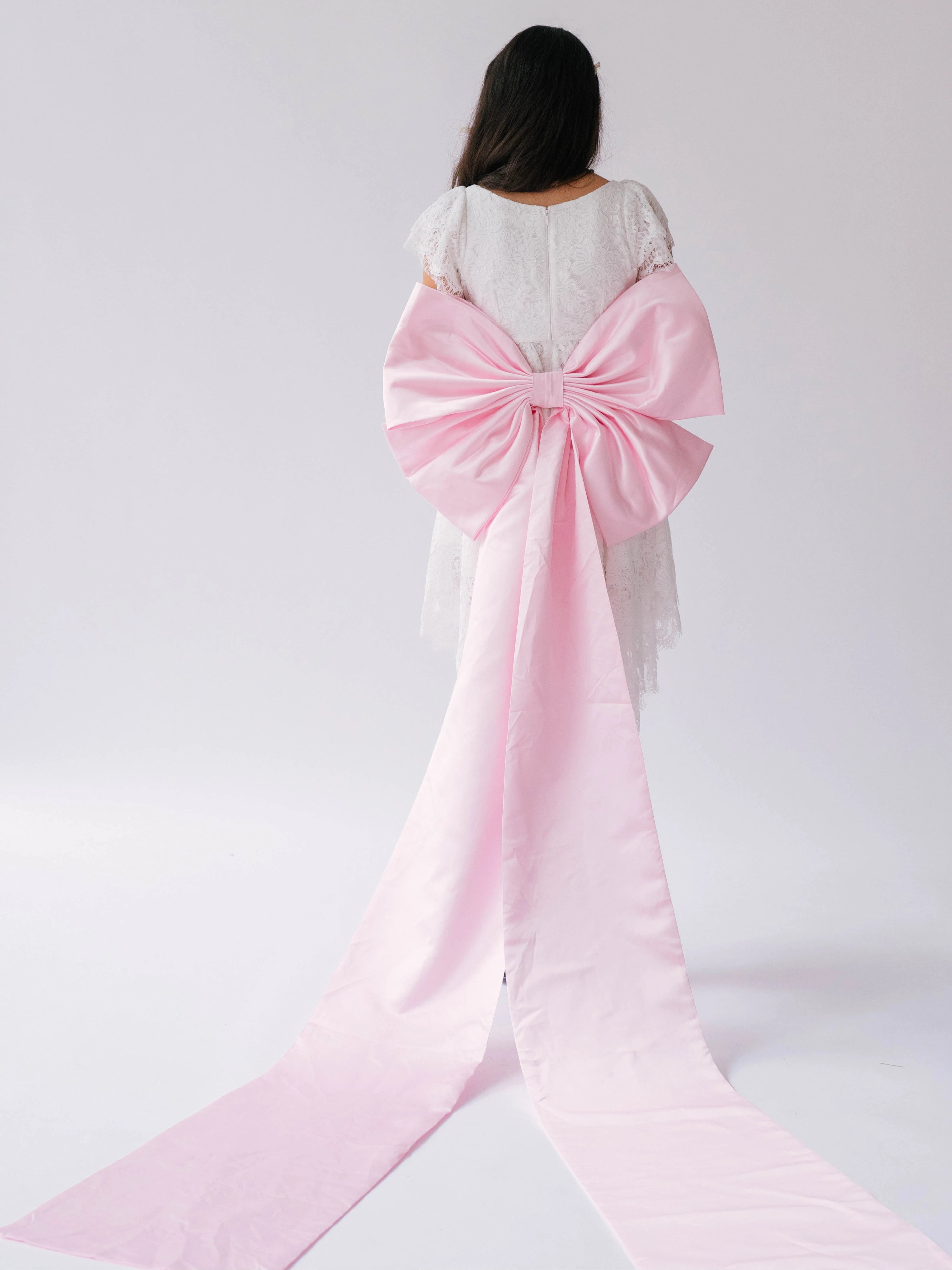 Pink satin large bow with long ribbons on a white bridal mini dress.