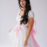 Woman wearing a white lace mini dress with short sleeves featuring a Ballet Pink Bow Sash Belt