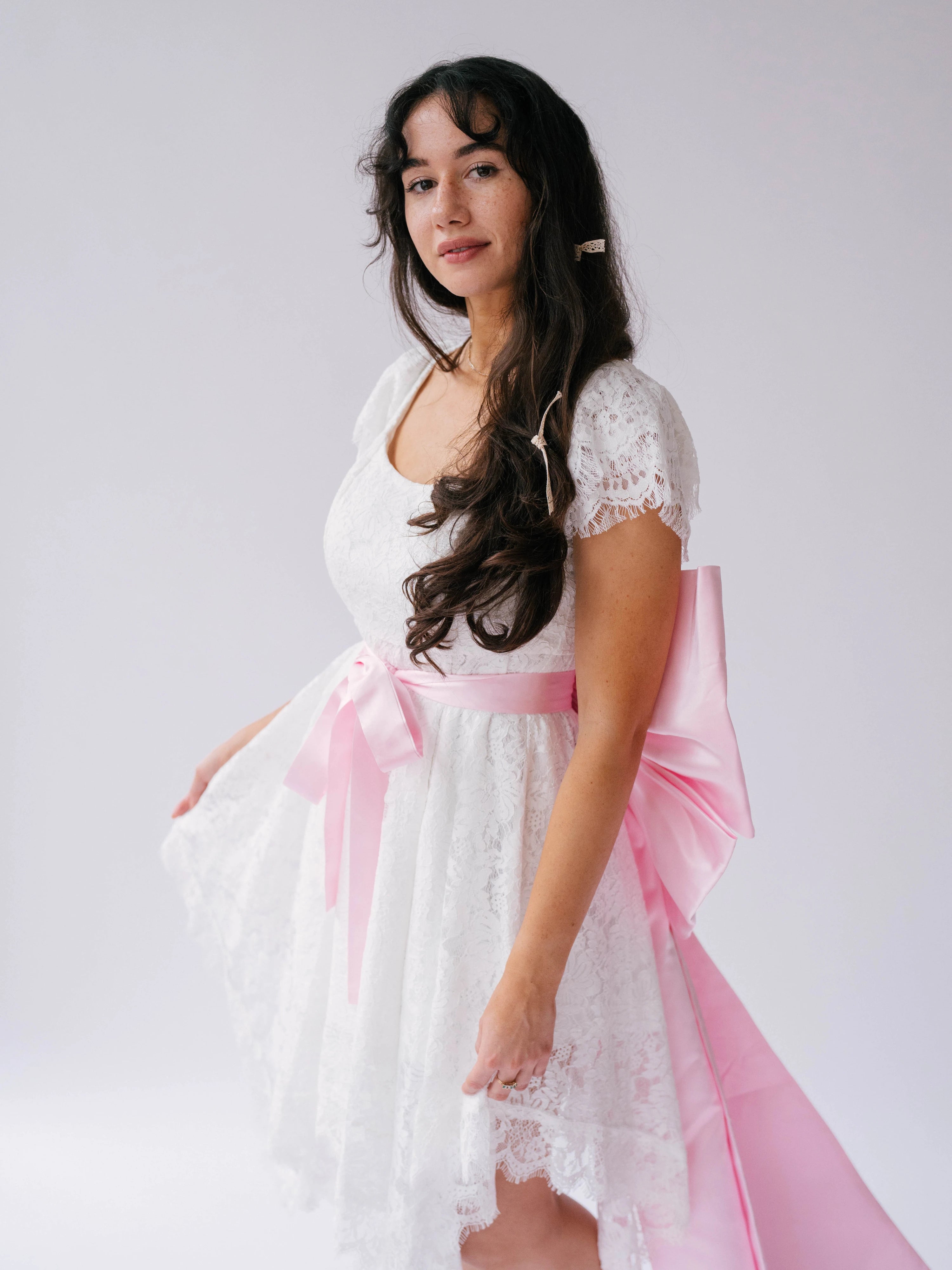 Woman wearing a white lace mini dress with short sleeves featuring a Ballet Pink Bow Sash Belt