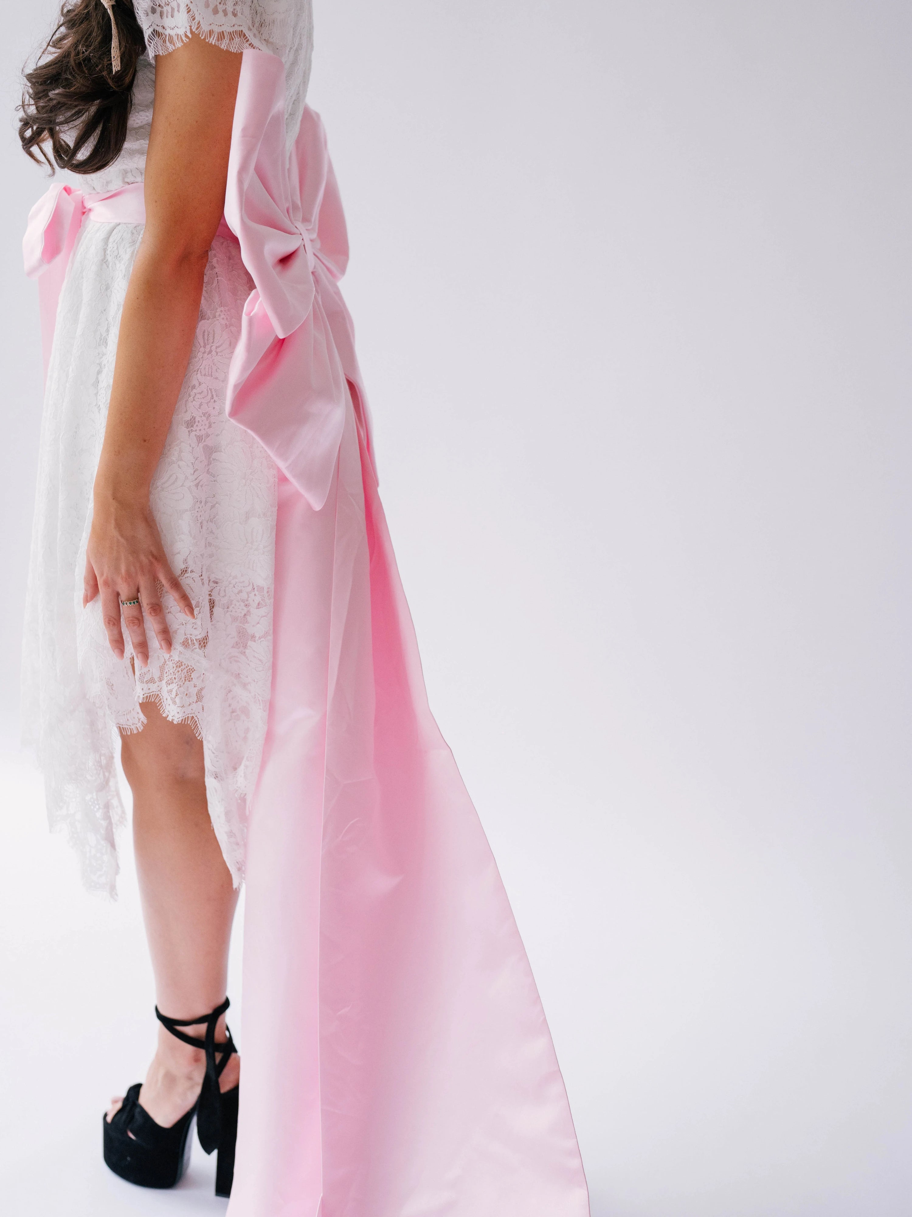 Woman wearing a white lace mini dress featuring the Ballet Pink Grand Bow Sash Belt