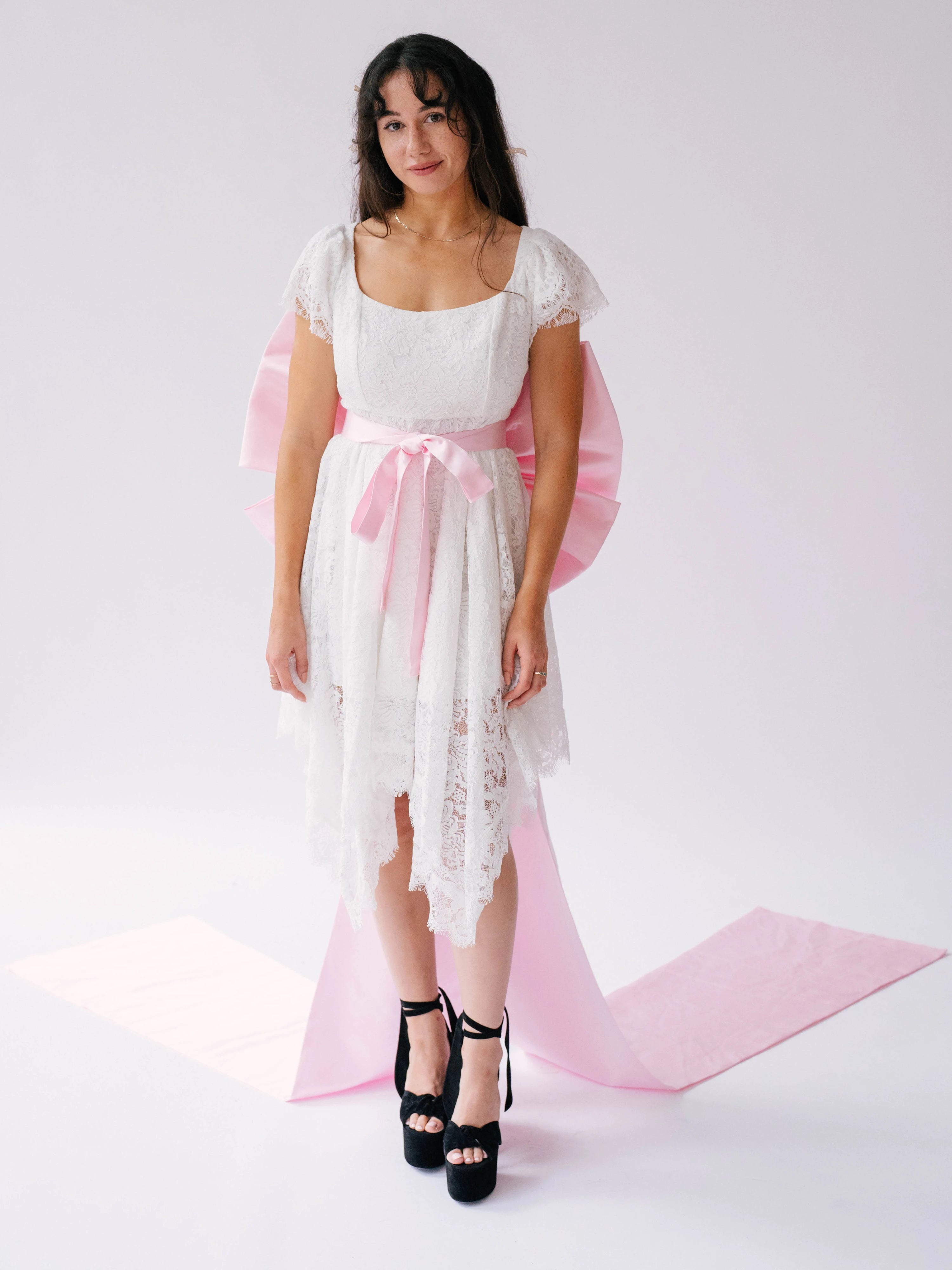 White lace dress with pink bow sash belt and black platform heels for a chic look