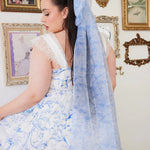 Blue Toile Grand Hair Bow with 36-inch tails styled in long hair, complementing a blue and white toile dress for a whimsical accessory look.