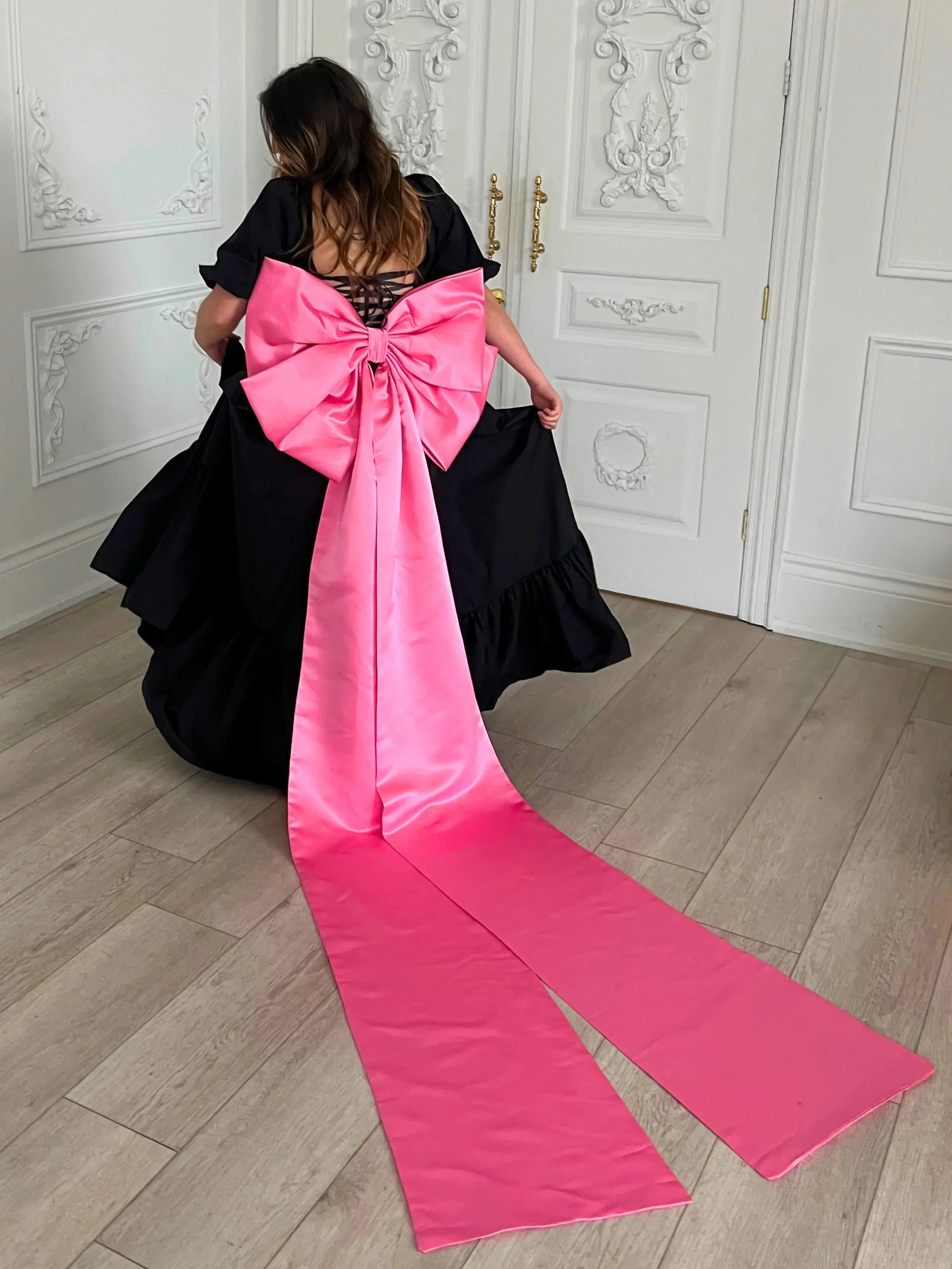 Bubblegum Pink Bow Belt with sculpted bow and sweeping tails styled on a voluminous black dress, ideal for Winter Drop 2023 fashion.