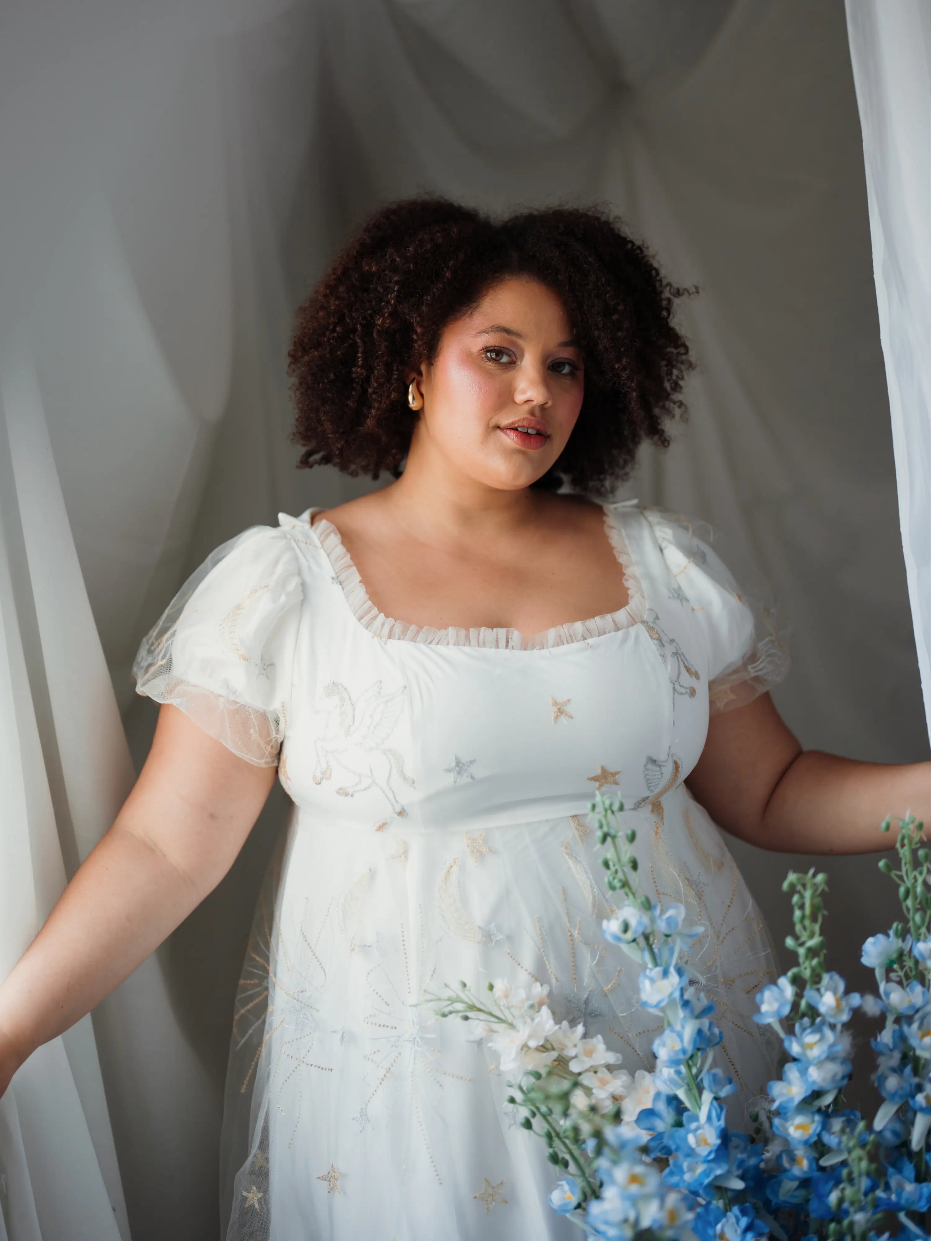Woman in a white dress standing next to flowers with a neutral background