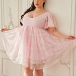 the Cherub Pink Lace Dress mini dress with angelic flutter sleeves and voluminous lace skirt, styled in a romantic vintage-inspired setting.