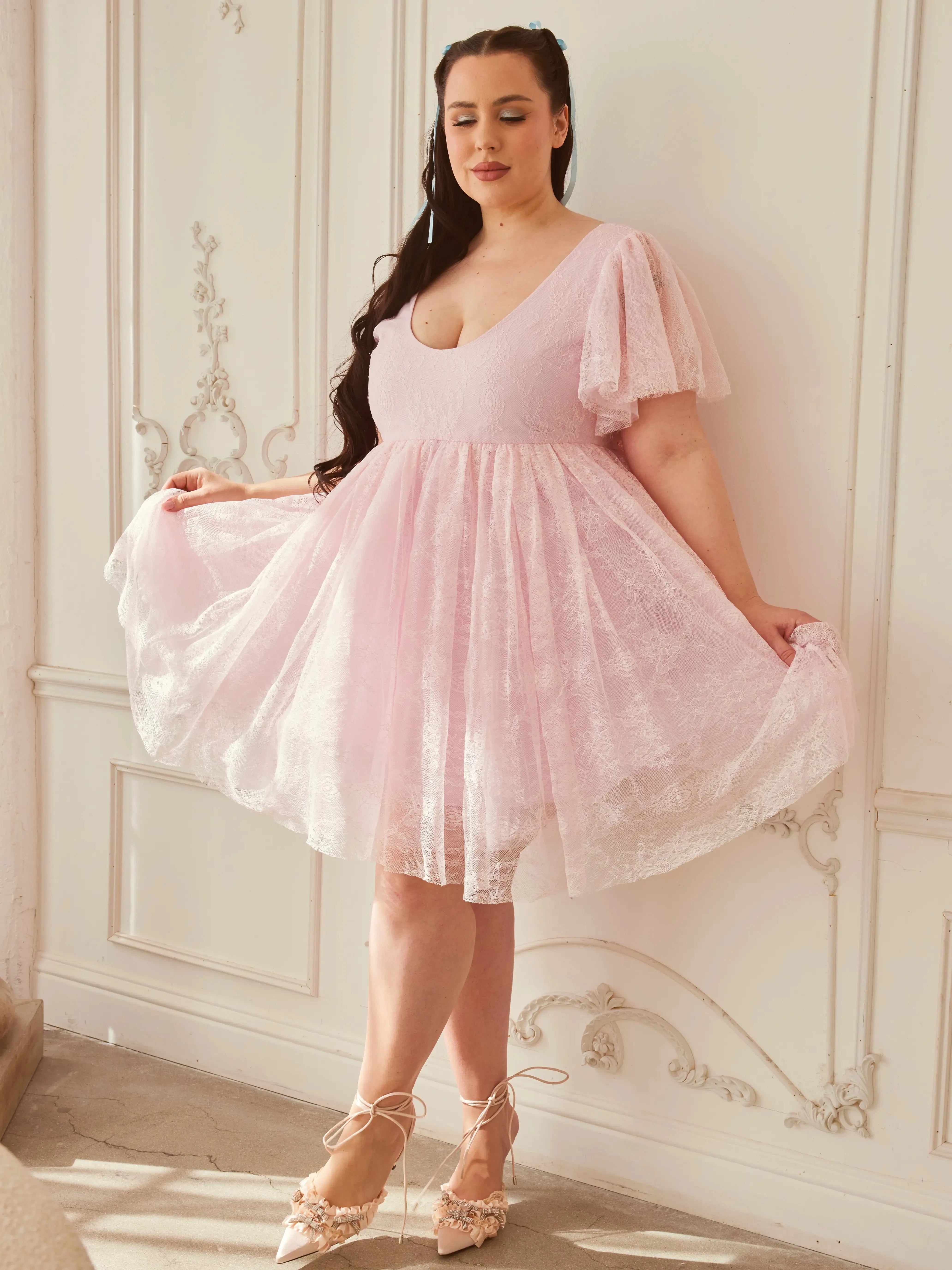 the Cherub Pink Lace Dress styled with lace-up heels, showcasing its flowy skirt and feminine silhouette in a vintage-inspired room.