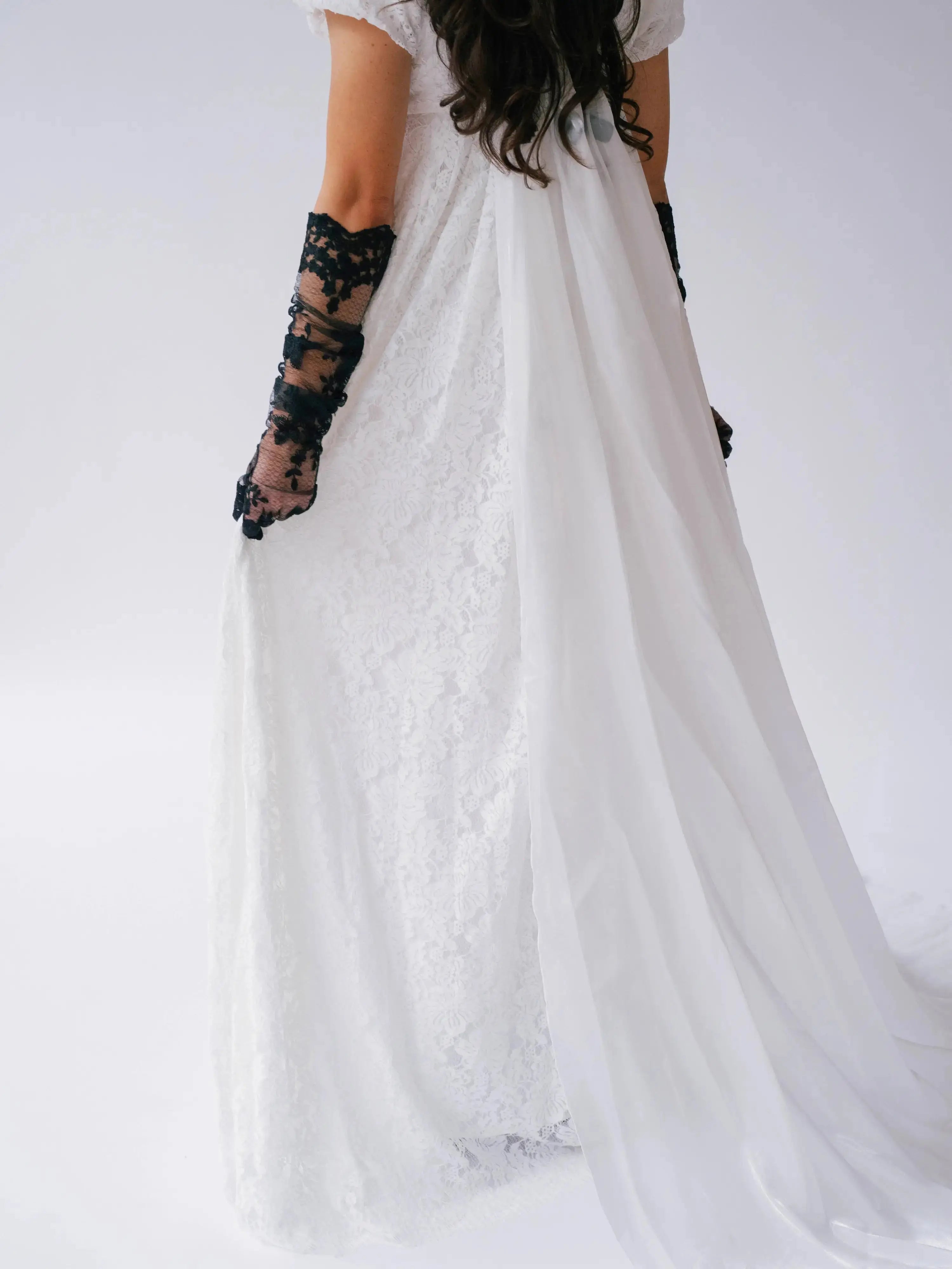 Back detail of Dauphine Lace Gown with sheer train and lace overlay, styled with black gloves for a bold bridal statement.