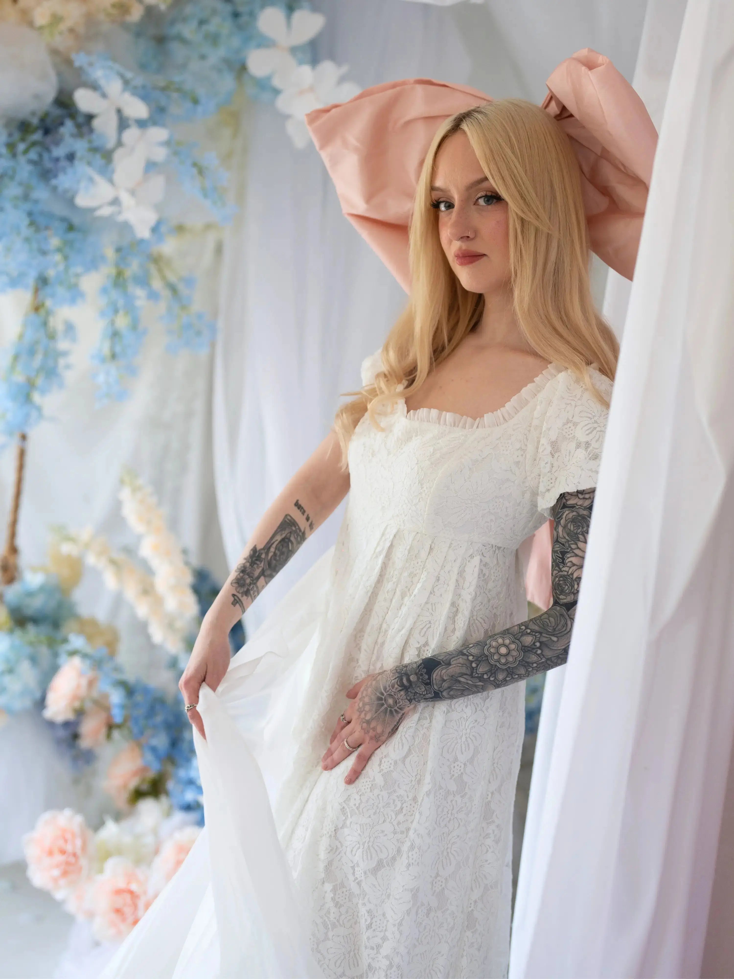 Romantic Dauphine Lace Gown with empire waist and soft lace, styled with oversized pink bow in a dreamy bridal setting.