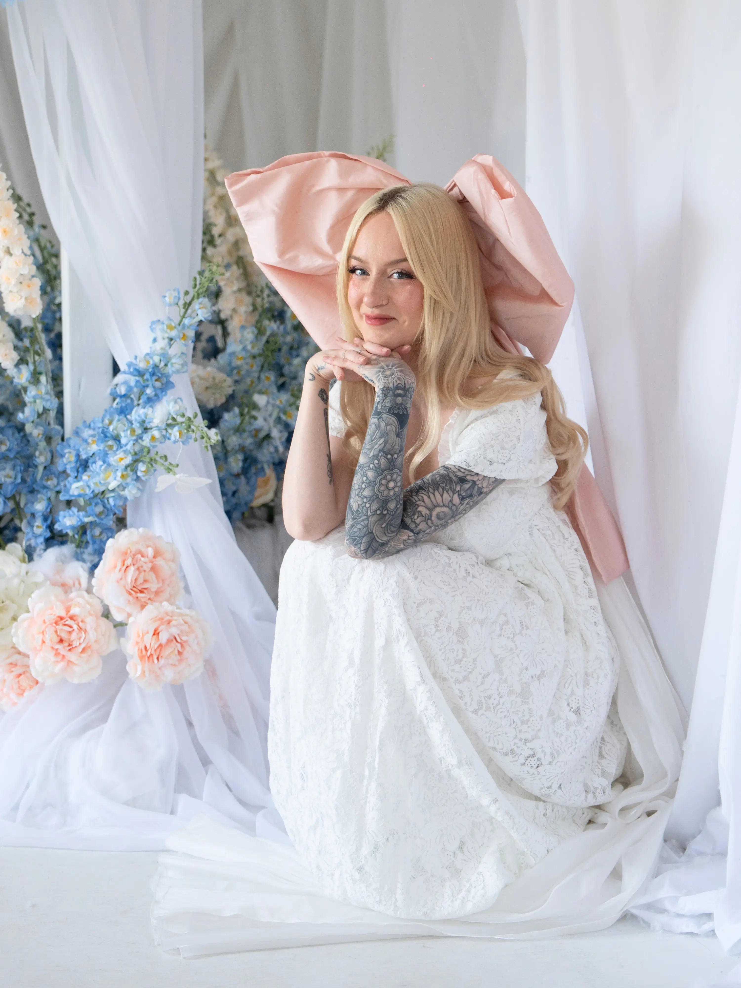 Model in Dauphine Lace Gown crouched in floral wedding scene, highlighting gown's lace detail and soft bridal aesthetic.
