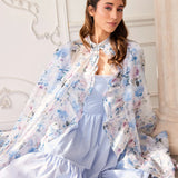 The High Priestess Renaissance Cloak draped elegantly over a seated model in a blue midi dress, emphasizing its princess core aesthetic.
