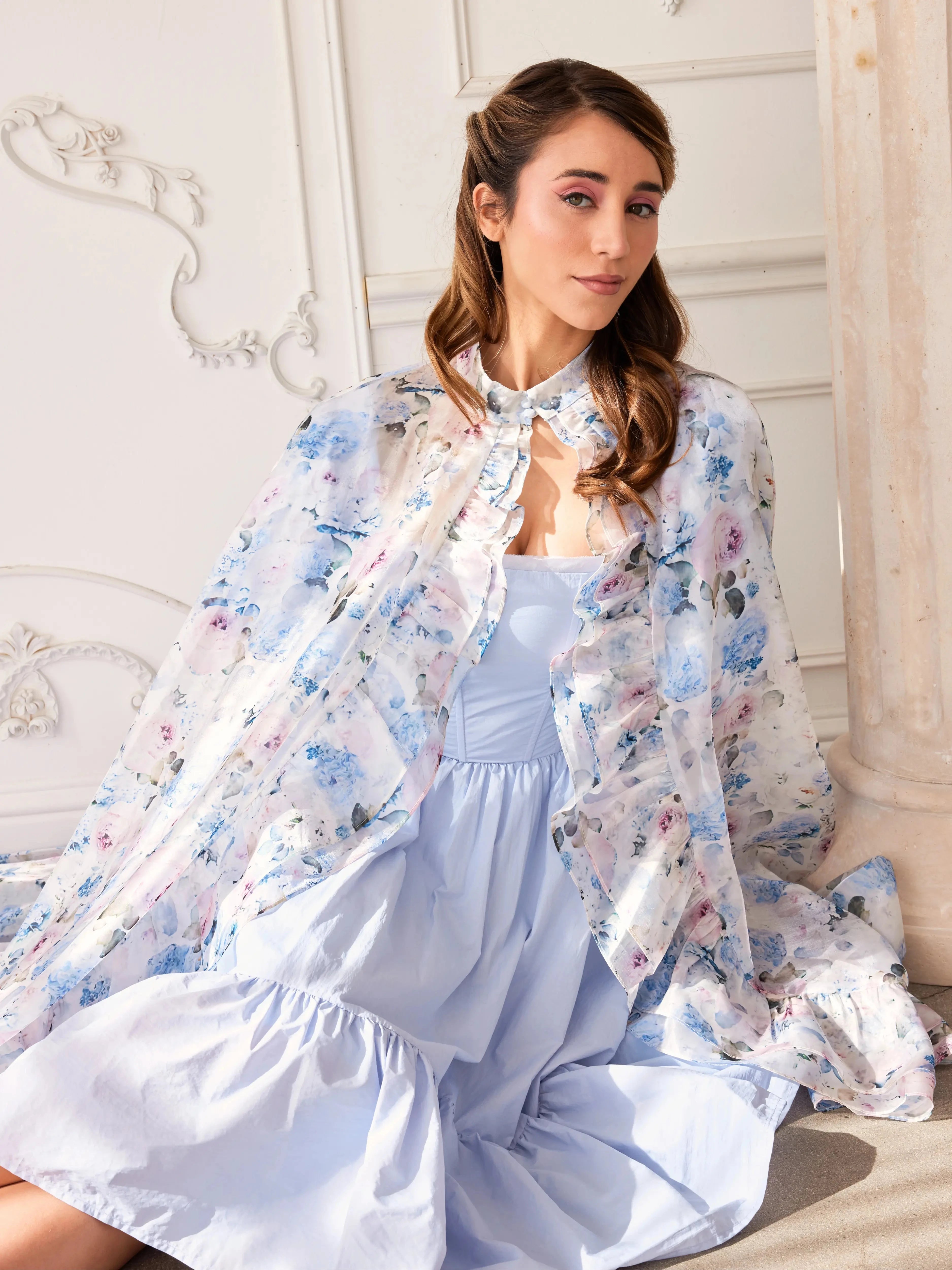 The High Priestess Renaissance Cloak draped elegantly over a seated model in a blue midi dress, emphasizing its princess core aesthetic.