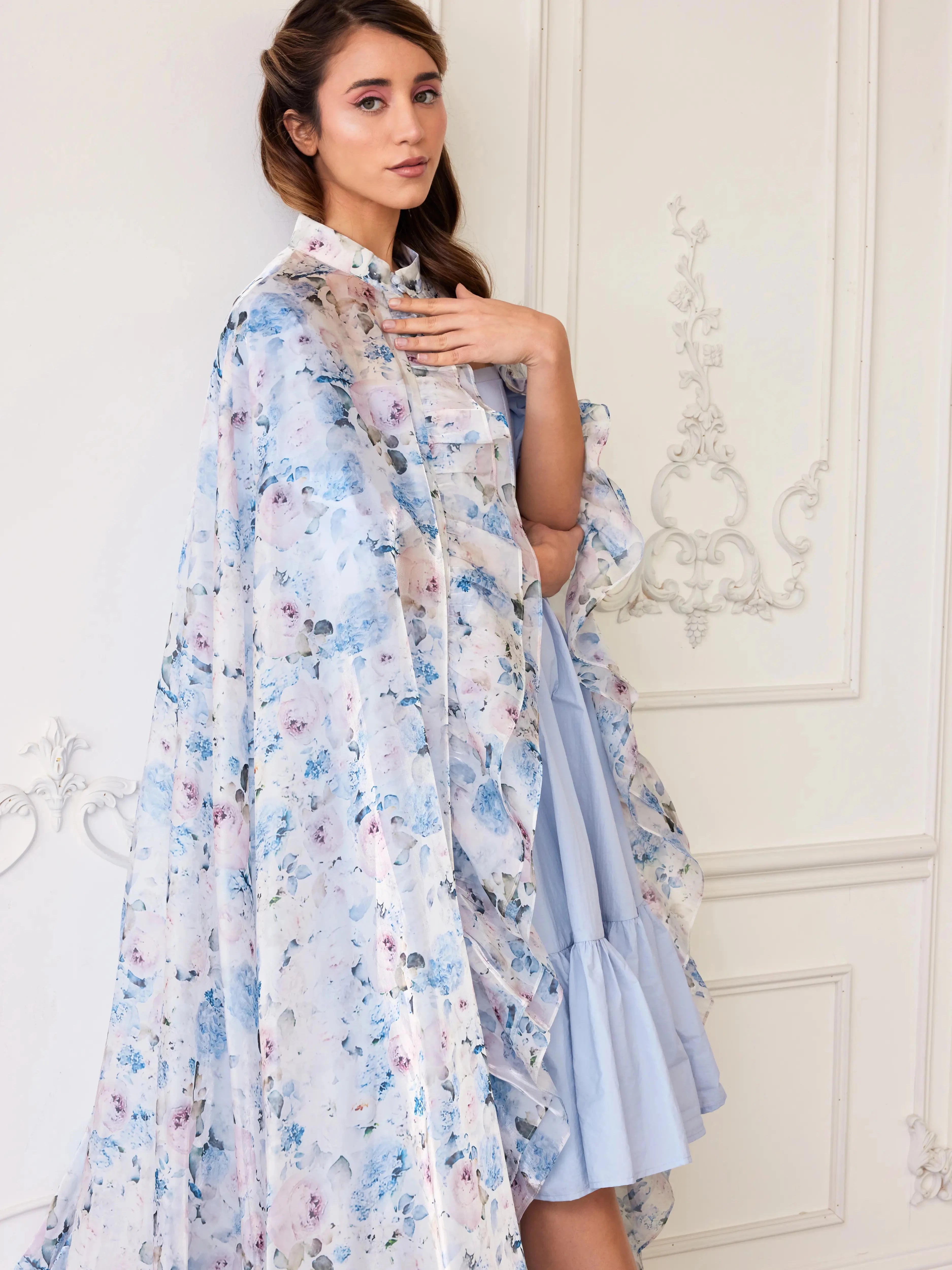 The High Priestess Renaissance Cloak worn over a pastel blue dress, highlighting the dreamy floral print and ruffled collar.
