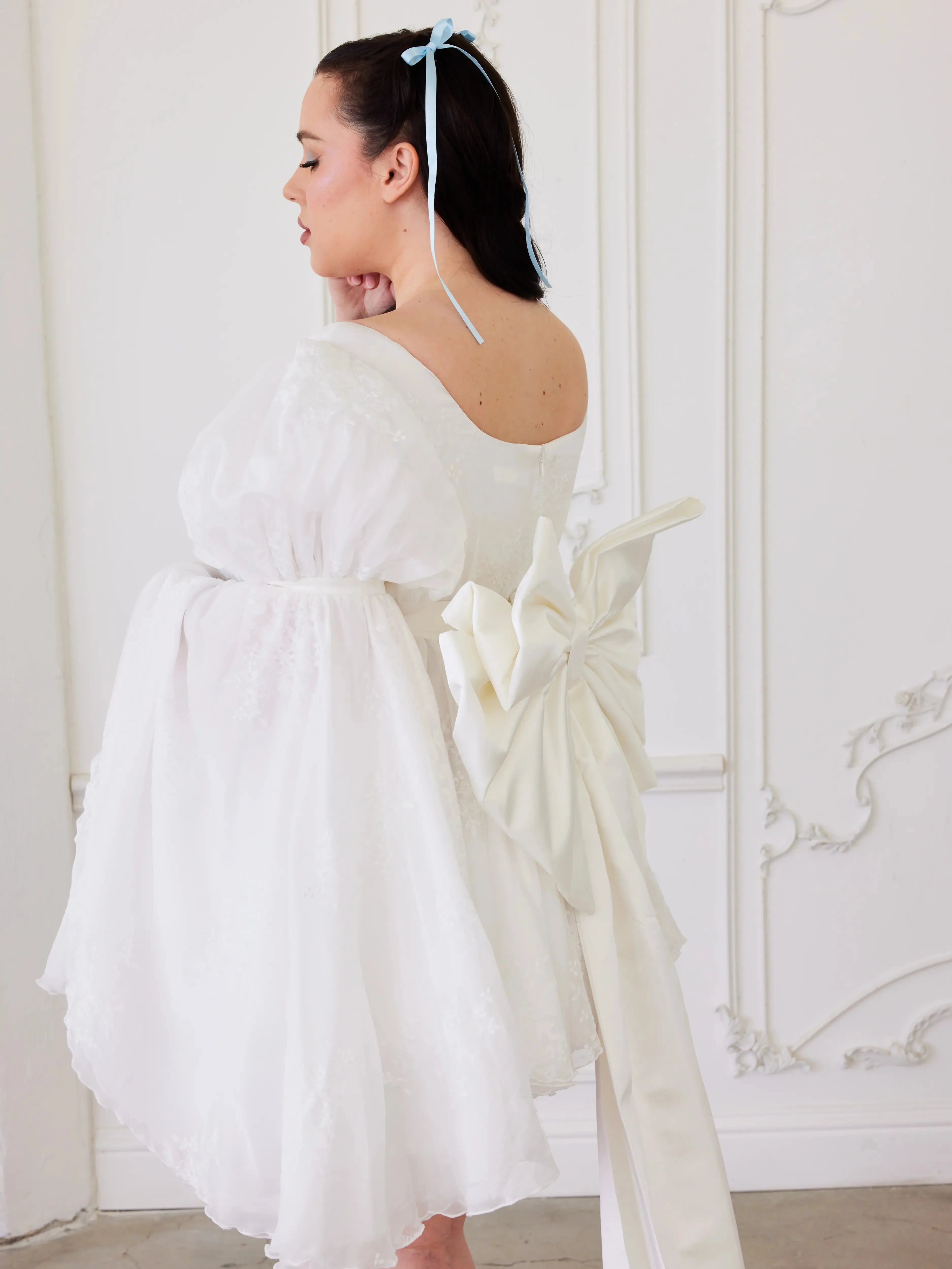 the Ivory Bridal Grand Bow Belt styled on a puff-sleeve mini wedding dress, highlighting its dramatic bow and cascading satin train.