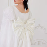 the Ivory Bridal Grand Bow Belt in white satin with oversized design and long train, styled on a short puff-sleeve bridal dress.