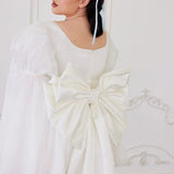 the Ivory Bridal Grand Bow Belt in white satin with oversized design and long train, styled on a short puff-sleeve bridal dress.