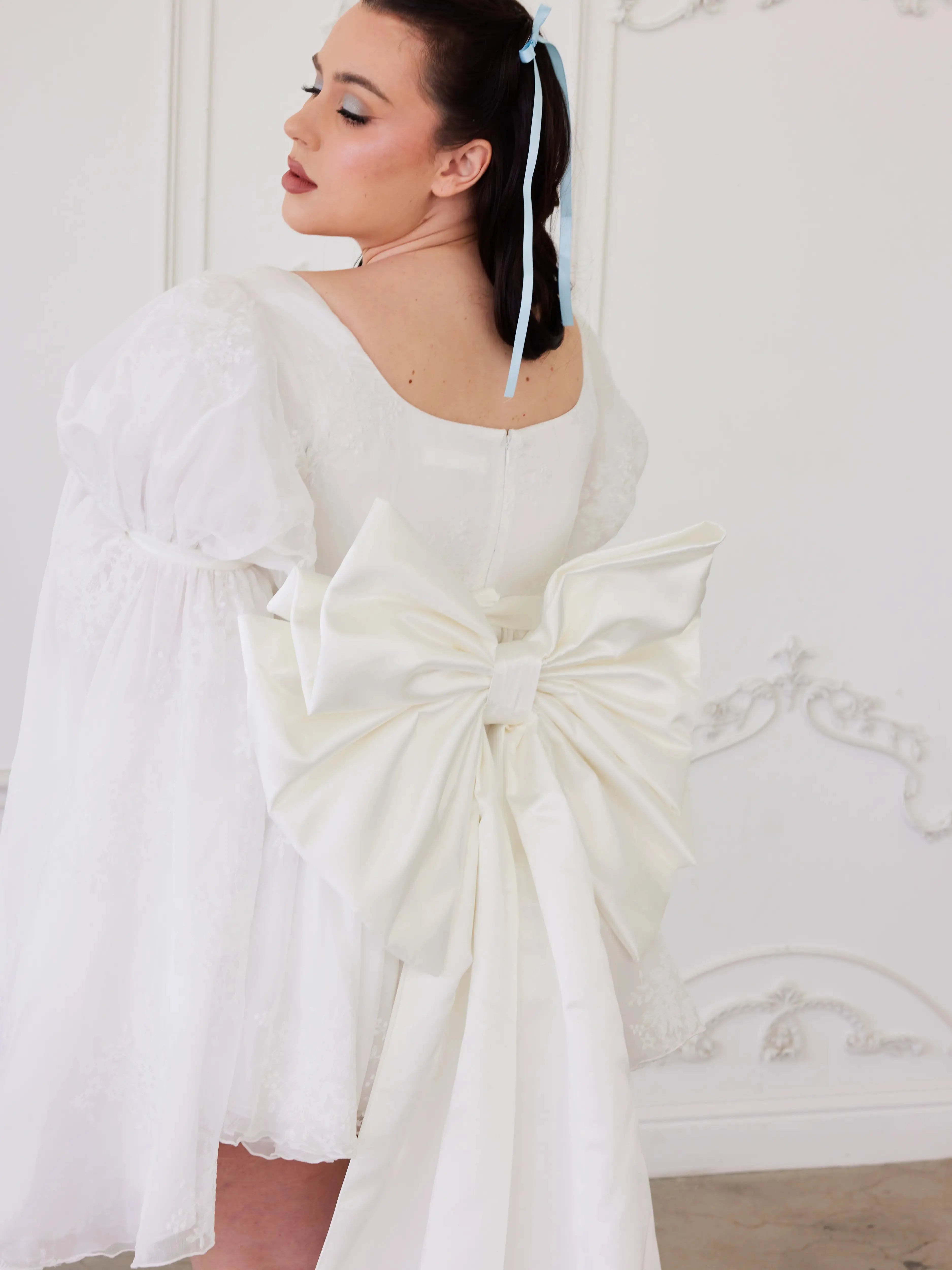 the Ivory Bridal Grand Bow Belt in white satin with oversized design and long train, styled on a short puff-sleeve bridal dress.