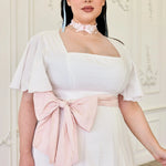 The Ivory Cloud Cotton Day Dress with soft pink waist bow and flutter sleeves, showcasing textured Swiss dot fabric for a vintage-inspired look.