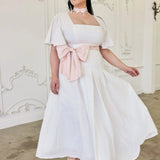 The Ivory Cloud Cotton Day Dress with pink sash and flutter sleeves, styled for summer weddings or romantic outings. Swiss dot texture adds elegance.