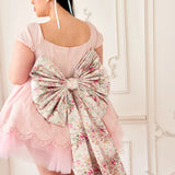 the Rosewater Grand Bow Belt in satin with custom rose print, styled on a pink lace dress. Features oversized bow and dramatic floral tails.