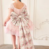 the Rosewater Grand Bow Belt with voluminous floral bow and extended satin tails, paired with a pink tulle dress and floral heels.