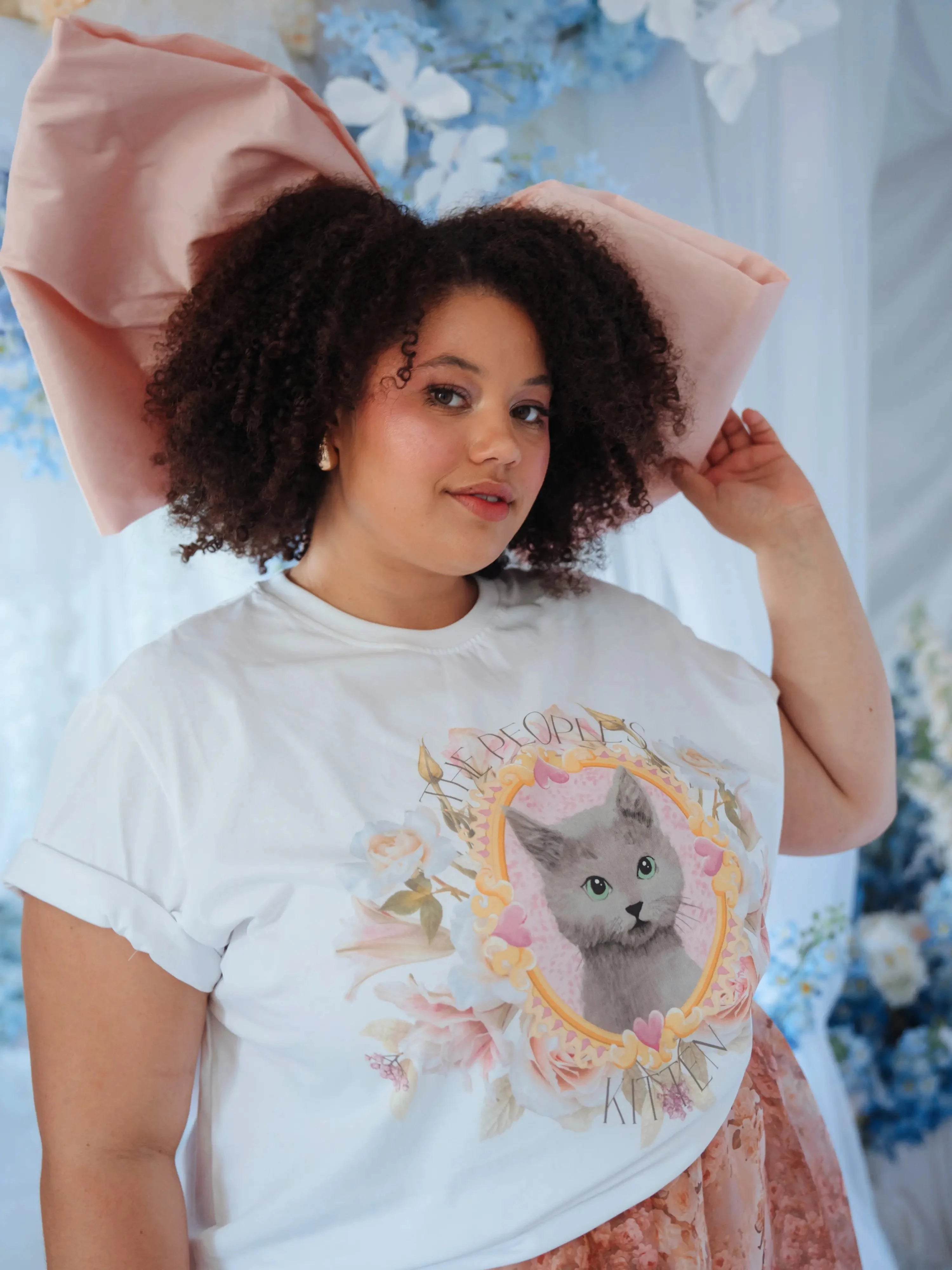 Model in The Princess Kitten Tee with oversized pink bow and floral skirt, emphasizing the tee’s playful and artistic kitten print.