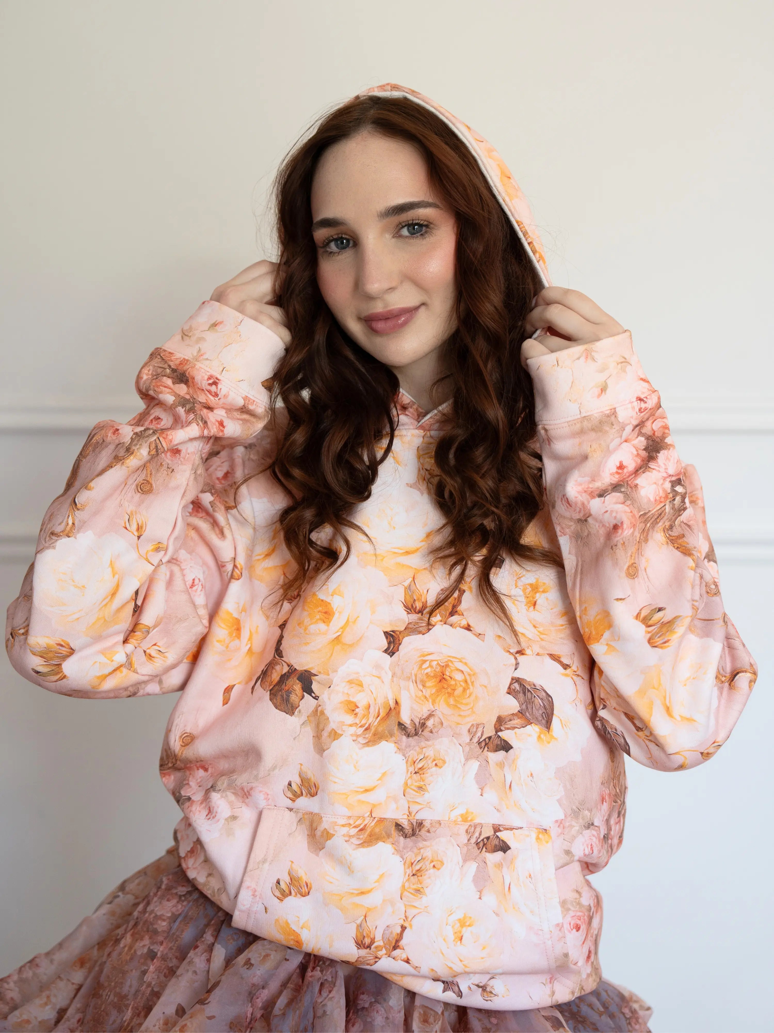 The Twilight Bloom Sleeper Hoodie featuring pastel rose patterns, worn with a ruffled skirt. Ideal for cozy, whimsical fashion in hoodie tops.