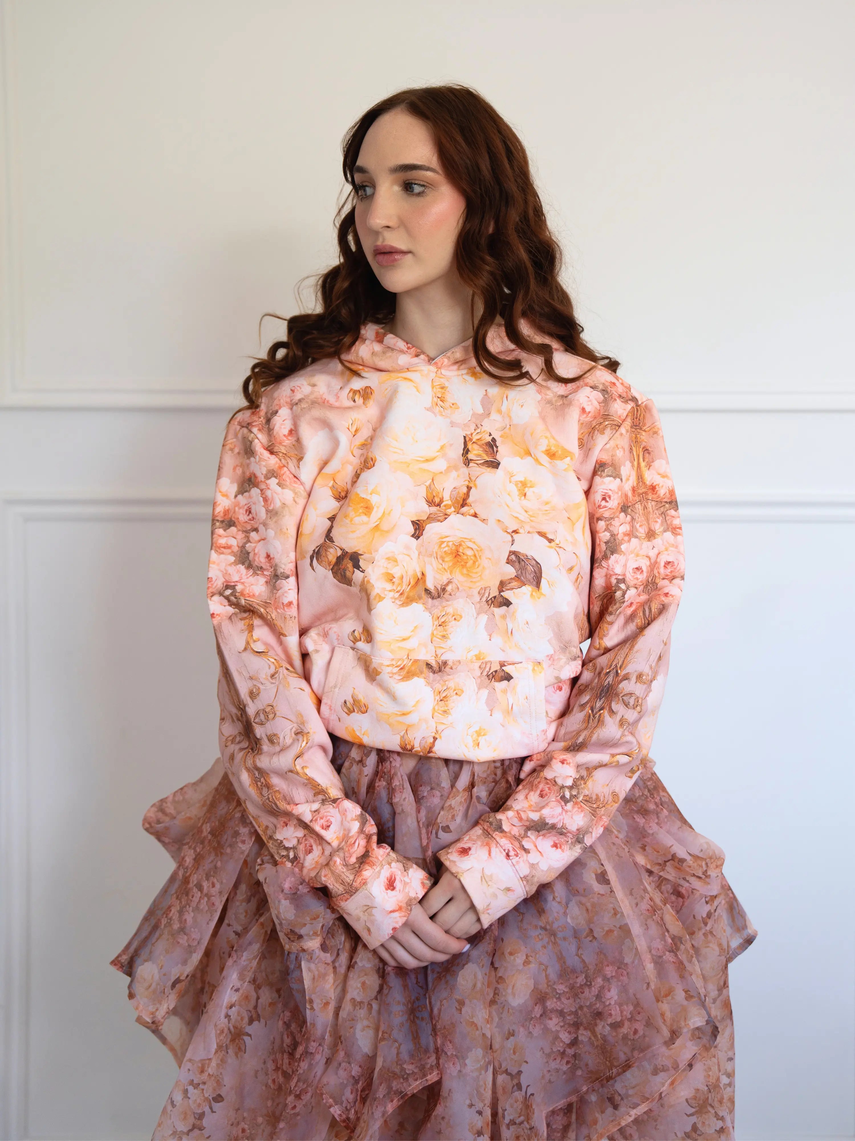 The Twilight Bloom Sleeper Hoodie styled with a layered floral skirt. Features soft pink tones and vintage rose design for cozy, feminine fashion.