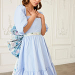 Front view of the Wildbloom Grand Bow Belt cinching a pastel blue dress, showcasing the floral waistband and voluminous silhouette.