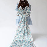 Back view of the Wildbloom Grand Bow Belt with dramatic floral bow and extended satin ribbons, styled on a tiered blue dress.