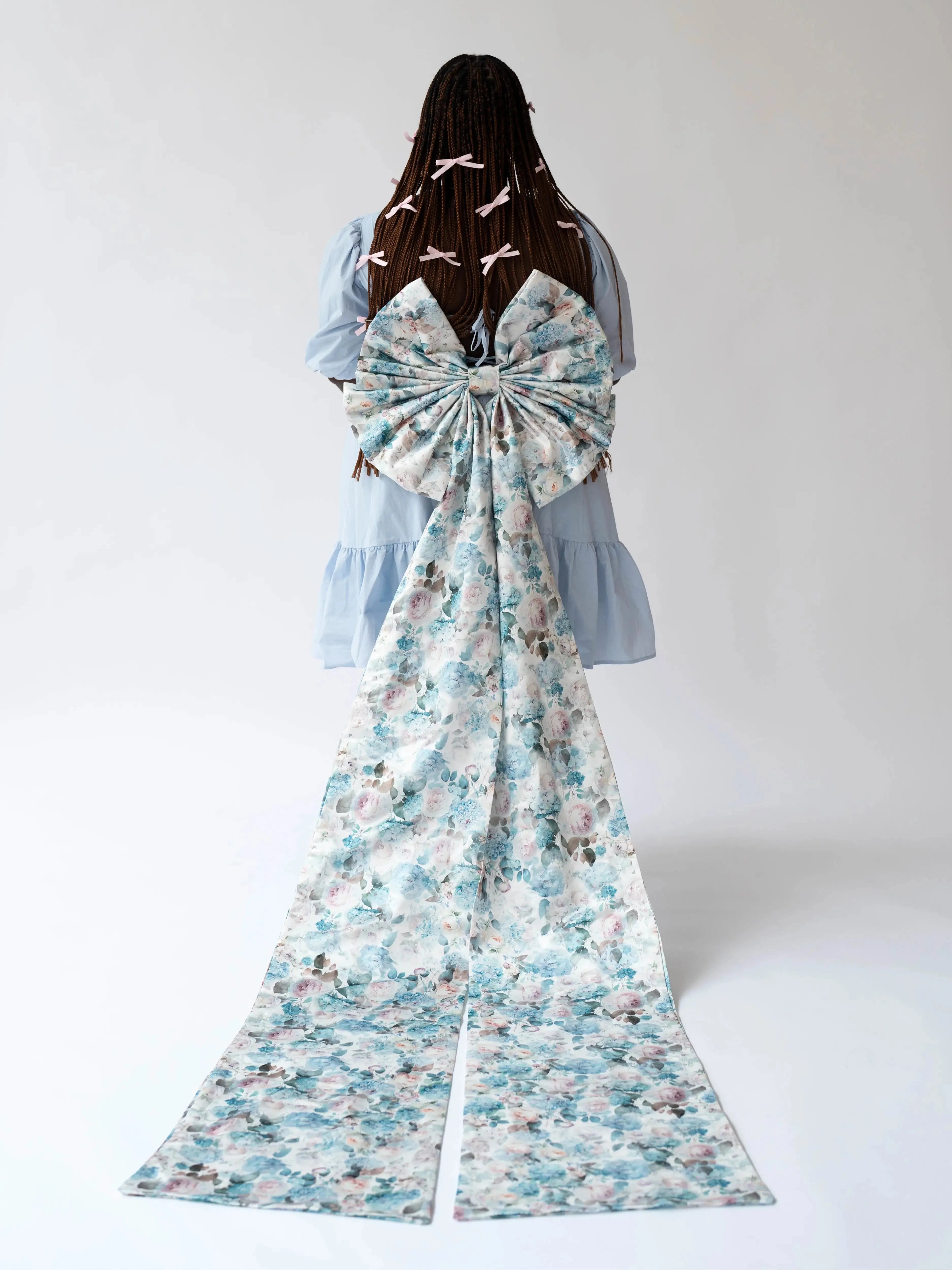 Back view of the Wildbloom Grand Bow Belt with dramatic floral bow and extended satin ribbons, styled on a tiered blue dress.