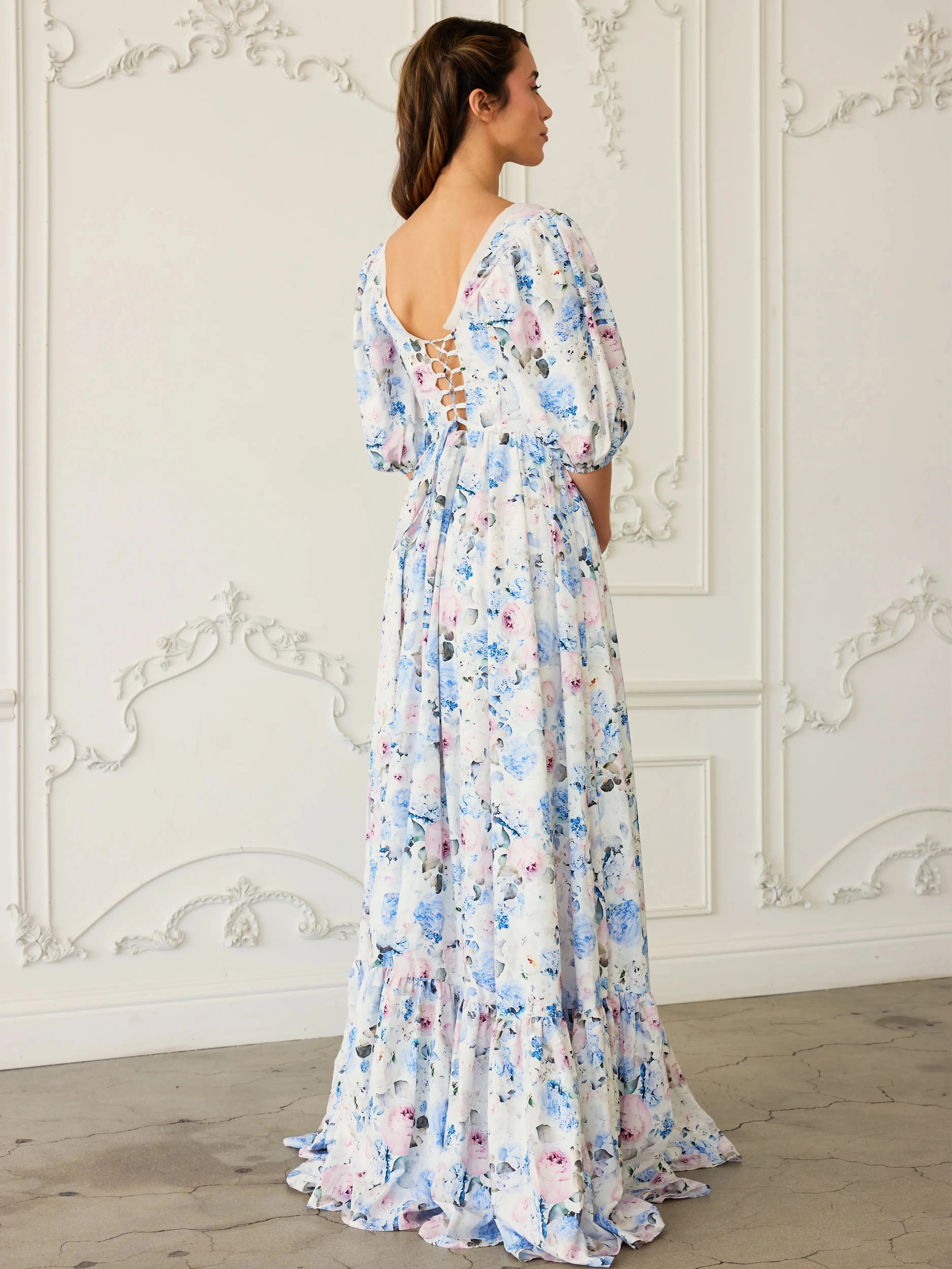 The Wildbloom Josephine Ball Gown photographed from behind showing the corset lacing and ruffled hem, styled in a white ornate room.