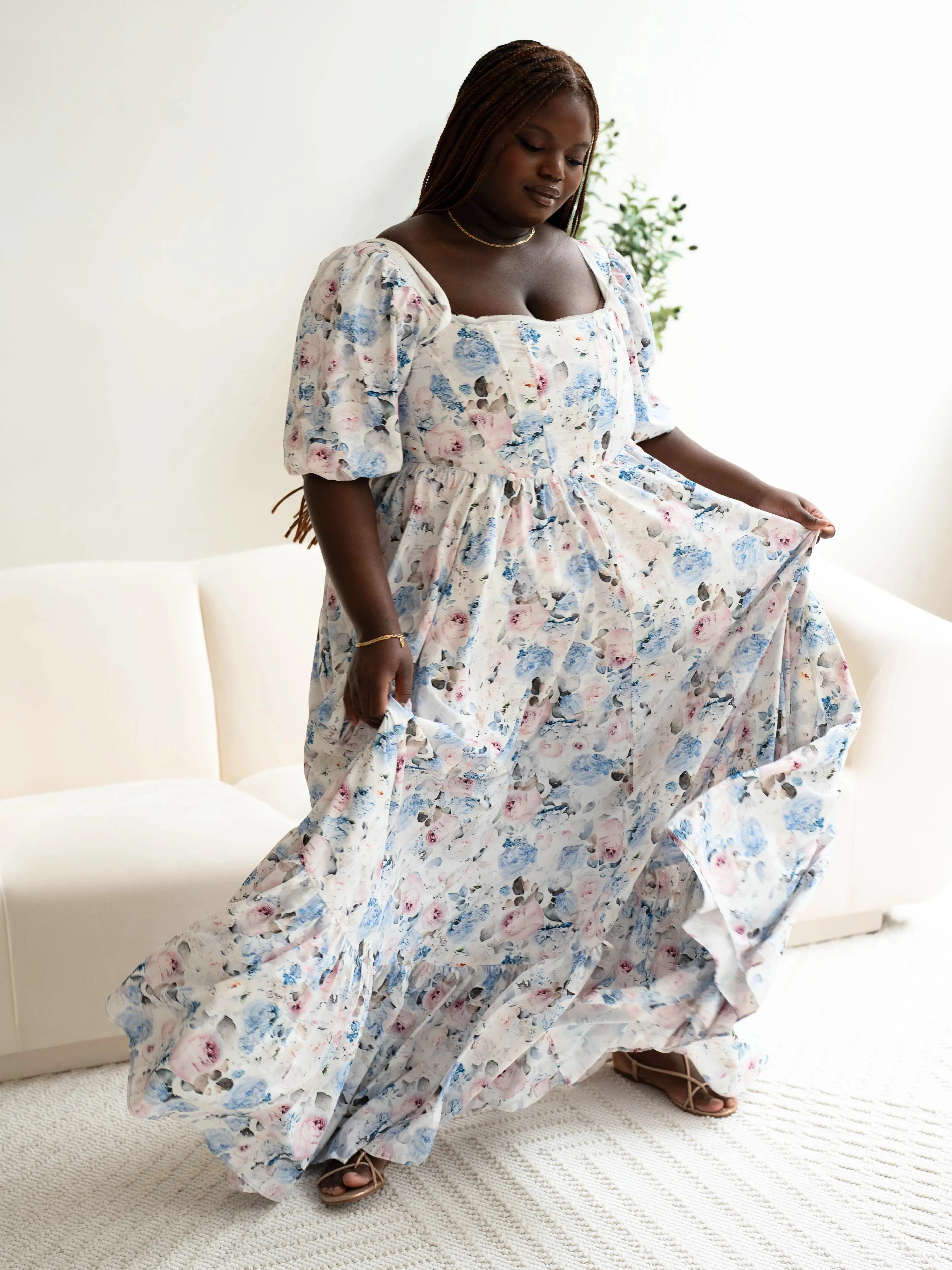 The Wildbloom Josephine Ball Gown, a floral Ball Gown with corset lacing and puff sleeves, modeled in a lounge setting.