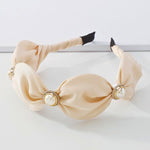 The Adorned Pearl Headband in ivory satin with large pearl and gold embellishments, perfect for elegant hair styling. Ideal for formal or bridal looks.