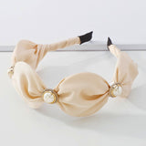 The Adorned Pearl Headband in ivory satin with large pearl and gold embellishments, perfect for elegant hair styling. Ideal for formal or bridal looks.