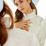 Caylee wearing the Alice Blue Grand Hair Bow styled with romantic waves and delicate lace attire, reflecting in a vintage mirror for a whimsical touch.