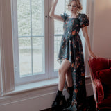 A woman in a taffeta dress is standing by a window in an elegant room.