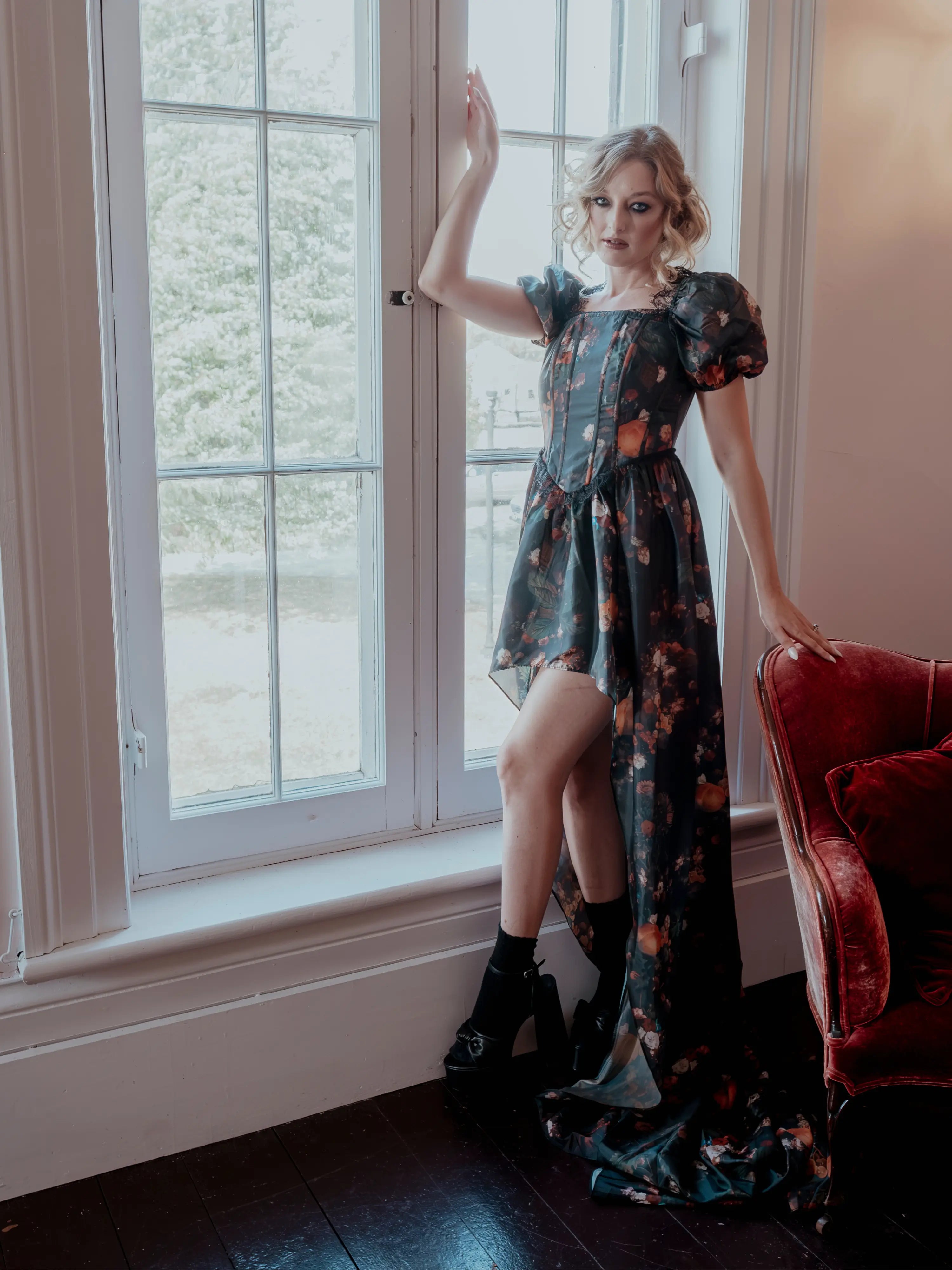 A woman in a taffeta dress is standing by a window in an elegant room.