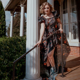 A woman wearing an autumn printed taffeta dress, standing on a porch with columns and a railing.