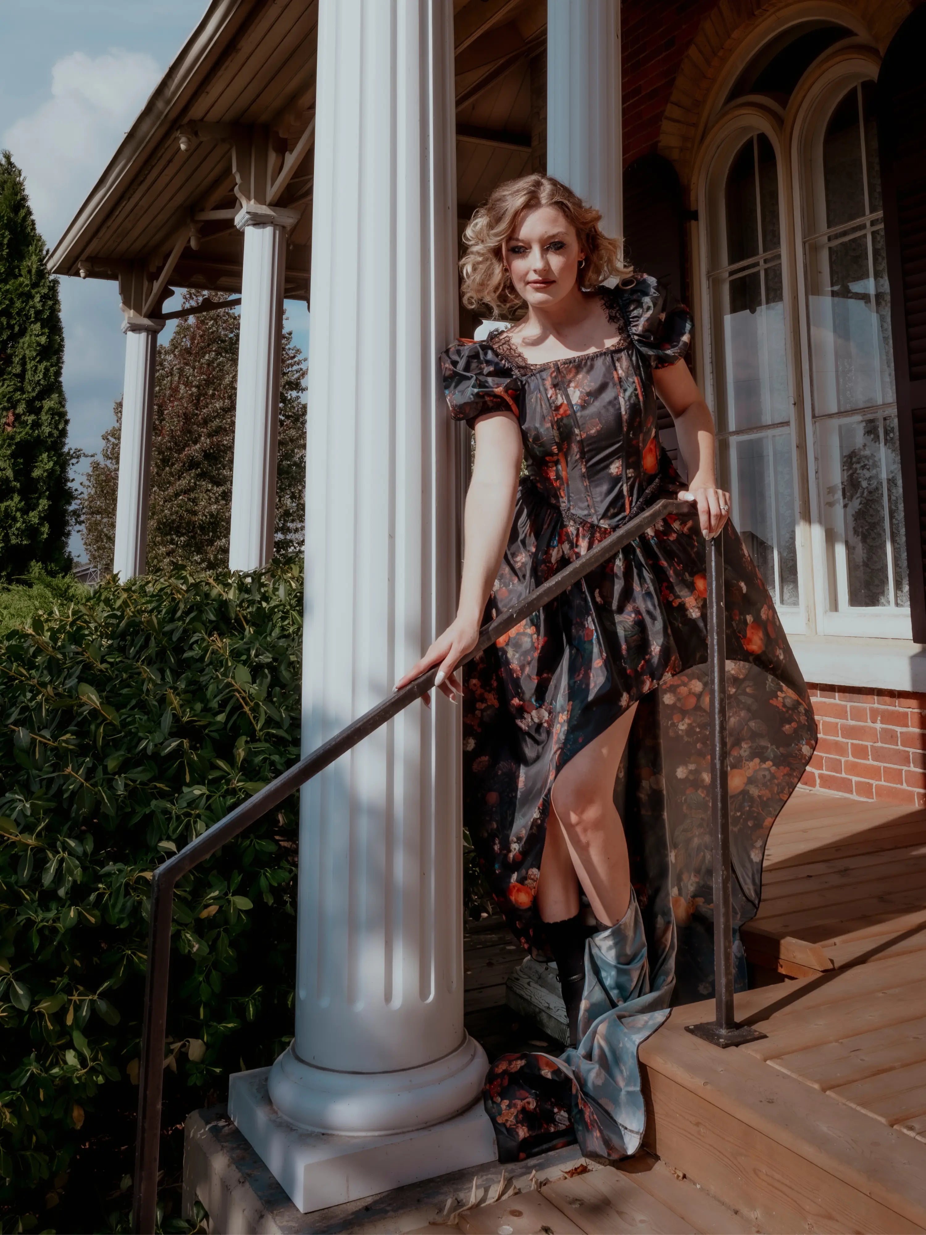 A woman wearing an autumn printed taffeta dress, standing on a porch with columns and a railing.