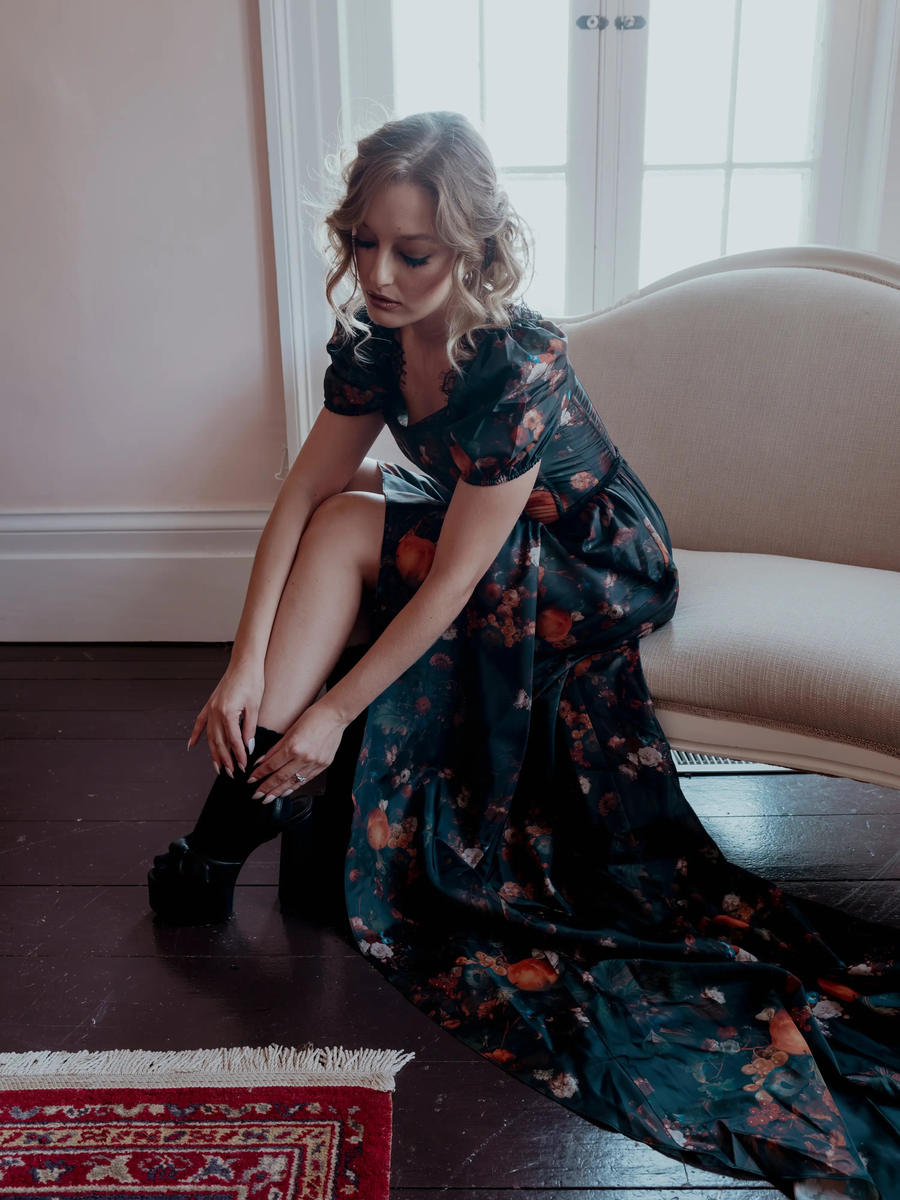 A woman wearing the still life Charlotte dress is sitting on the couch.
