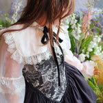 Close up view of a woman wearing a white shrug over a black corset dress in a floral setting.