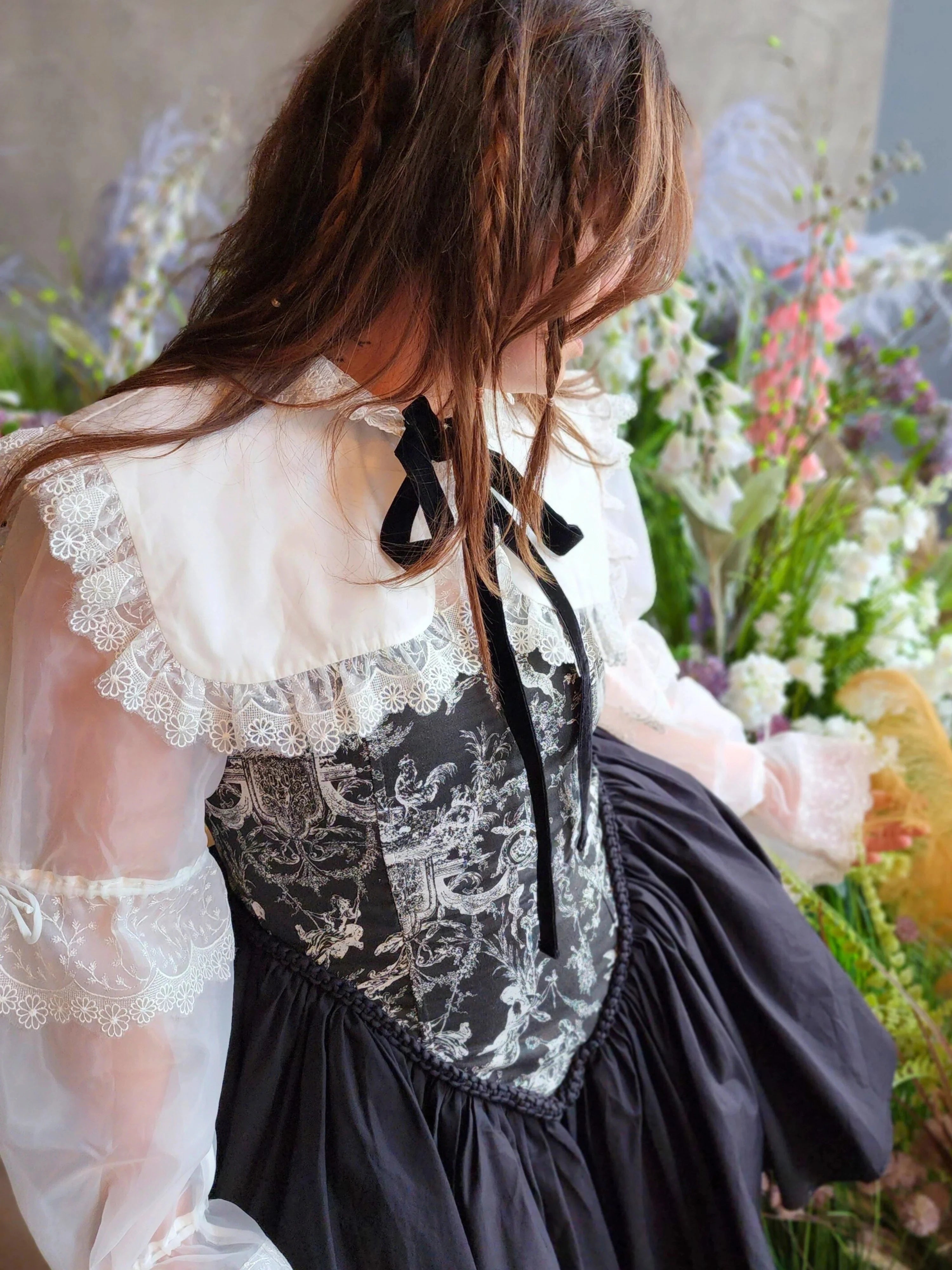 Close up view of a woman wearing a white shrug over a black corset dress in a floral setting.