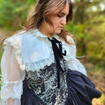 Side view of a woman wearing a black corset dress with a white shrug overtop in an outdoor setting.