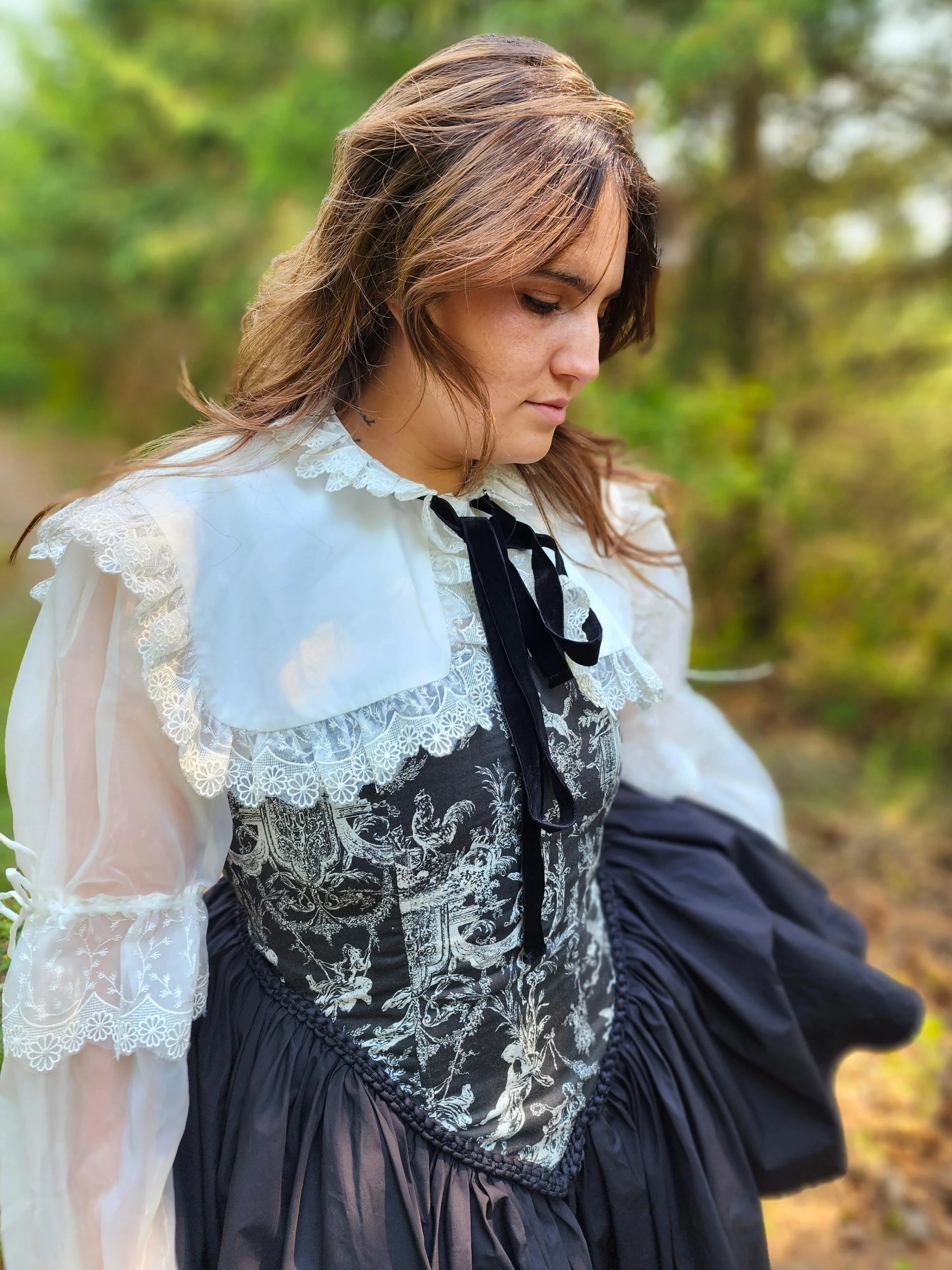 Side view of a woman wearing a black corset dress with a white shrug overtop in an outdoor setting.