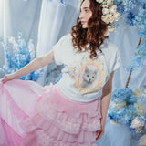 A woman wearing the dahlia pink ruffle skirt styled in a floral fantasy scene, featuring pink tulle ruffles and a flowing detachable train.